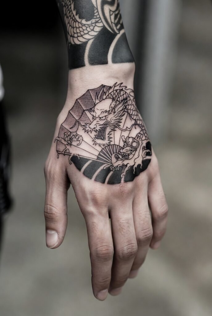 20+ Best Japanese Hand Tattoos: My Personal Favorites 2026 9 A close-up photograph of a Japanese dragon and flower tattoo on a hand, framed by a softly blurred indoor setting. Japanese hand tattoos