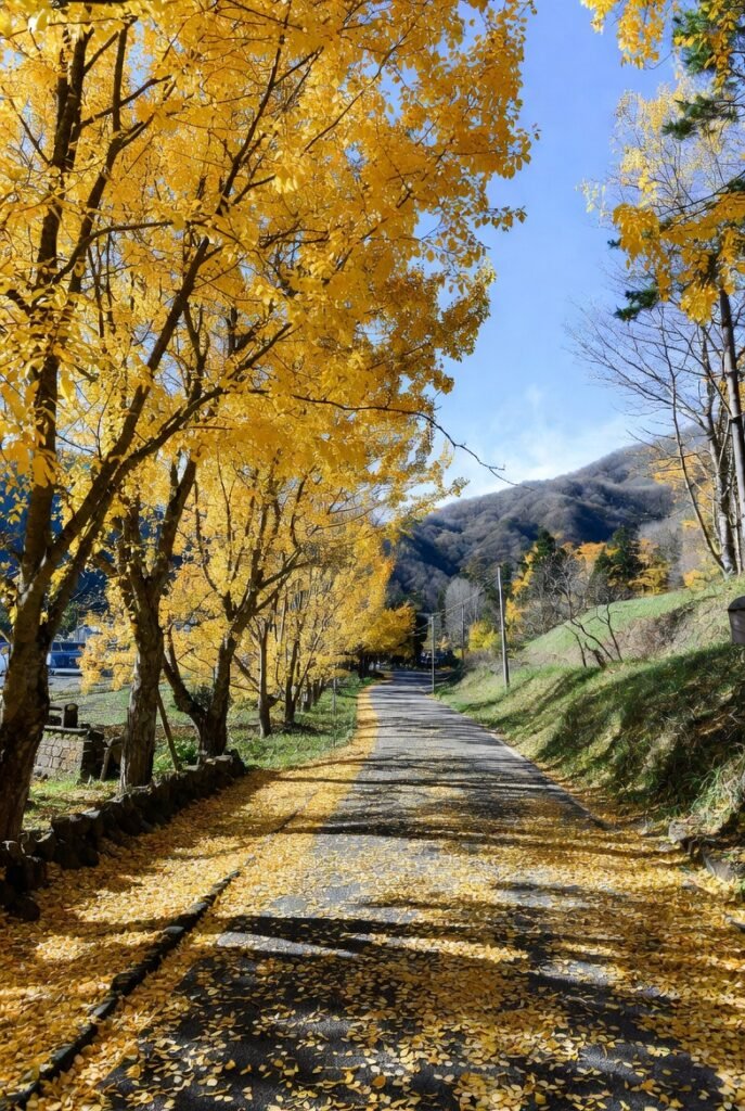 A lifelike autumn view from Yellow Spring Road in Japan, where trees with yellow leaves and stone lanterns border a road leading to traditional architecture.
