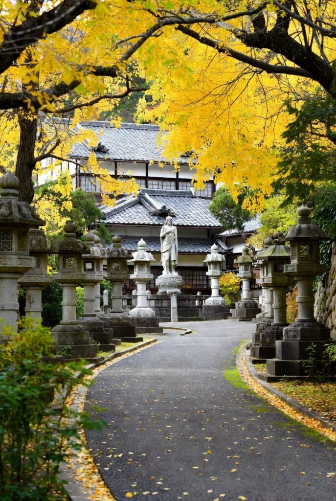 A photo of autumn on Yellow Spring Road, Japan, featuring yellow trees, fallen leaves, and stone lanterns in front of Japanese-style architecture.
