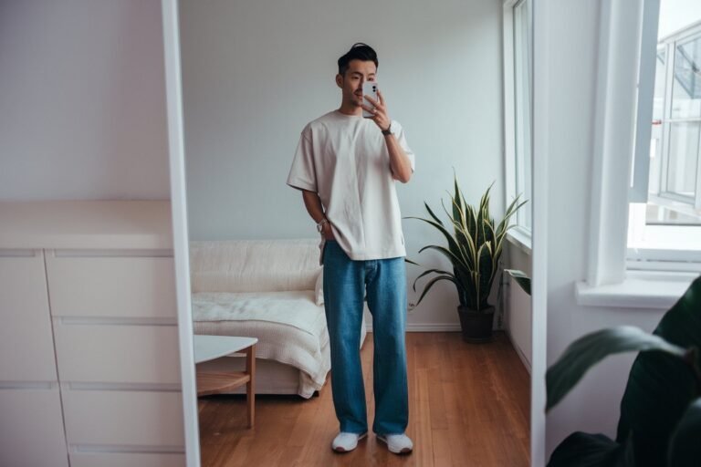 Japanese man taking a mirror selfie wearing a loose neutral t-shirt with straight-leg denim pants, clean bright interior — japanese mens casual everyday style.
