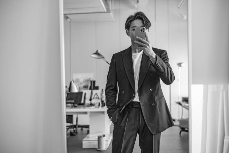 Japanese Mens Business Casual: 10 Modern Office-Ready Styles 2026! 25 Japanese man taking a mirror selfie wearing monochrome business-casual streetwear with tailored trousers and a structured blazer, clean minimal interior — japanese mens business casual.